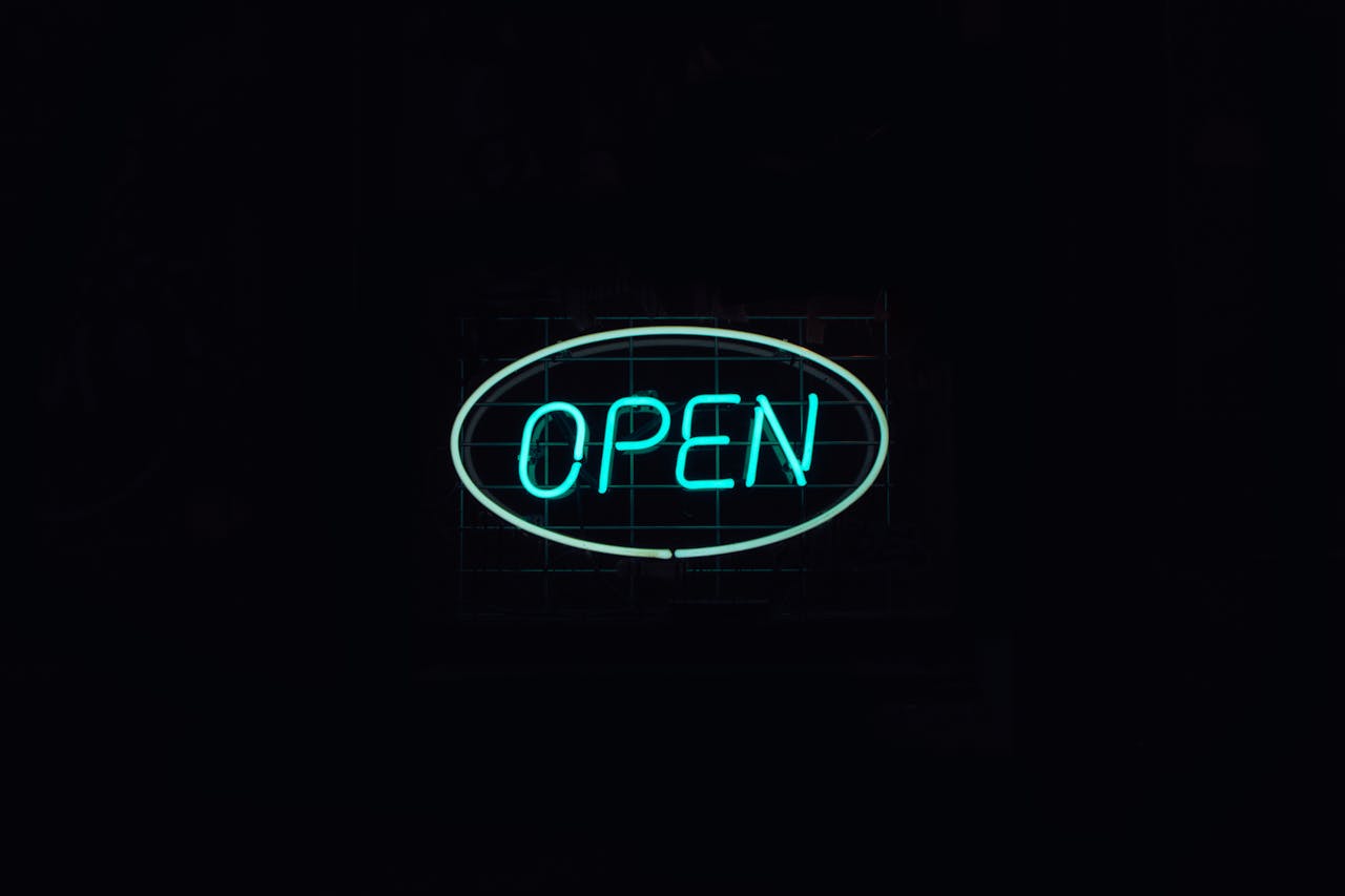 A vibrant neon 'Open' sign glows against a dark backdrop, ideal for business promotions.